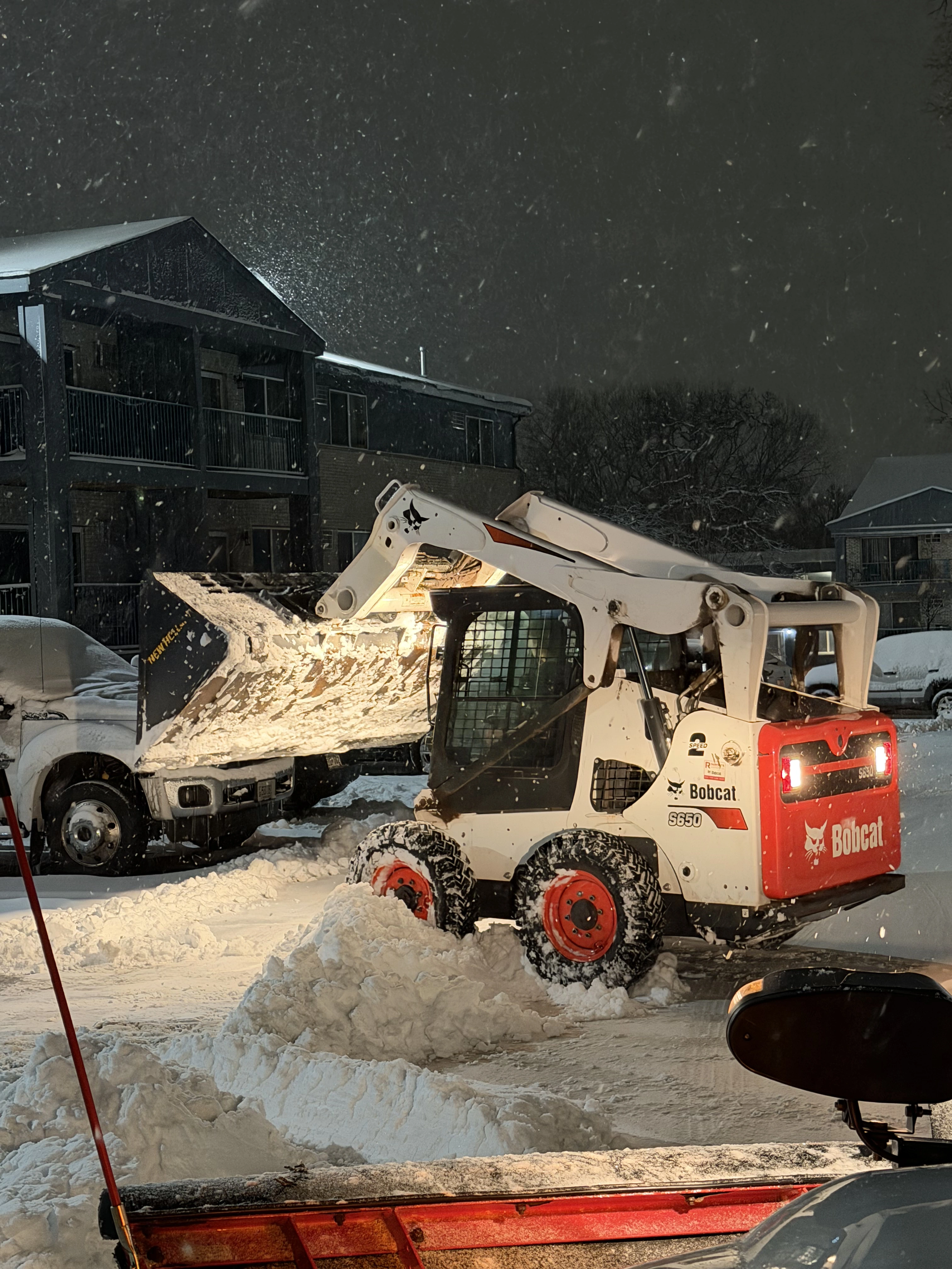 Bobcat skid steer clearing snow at a multifamily property parking lot during a night snowstorm in the North Twin Cities Metro