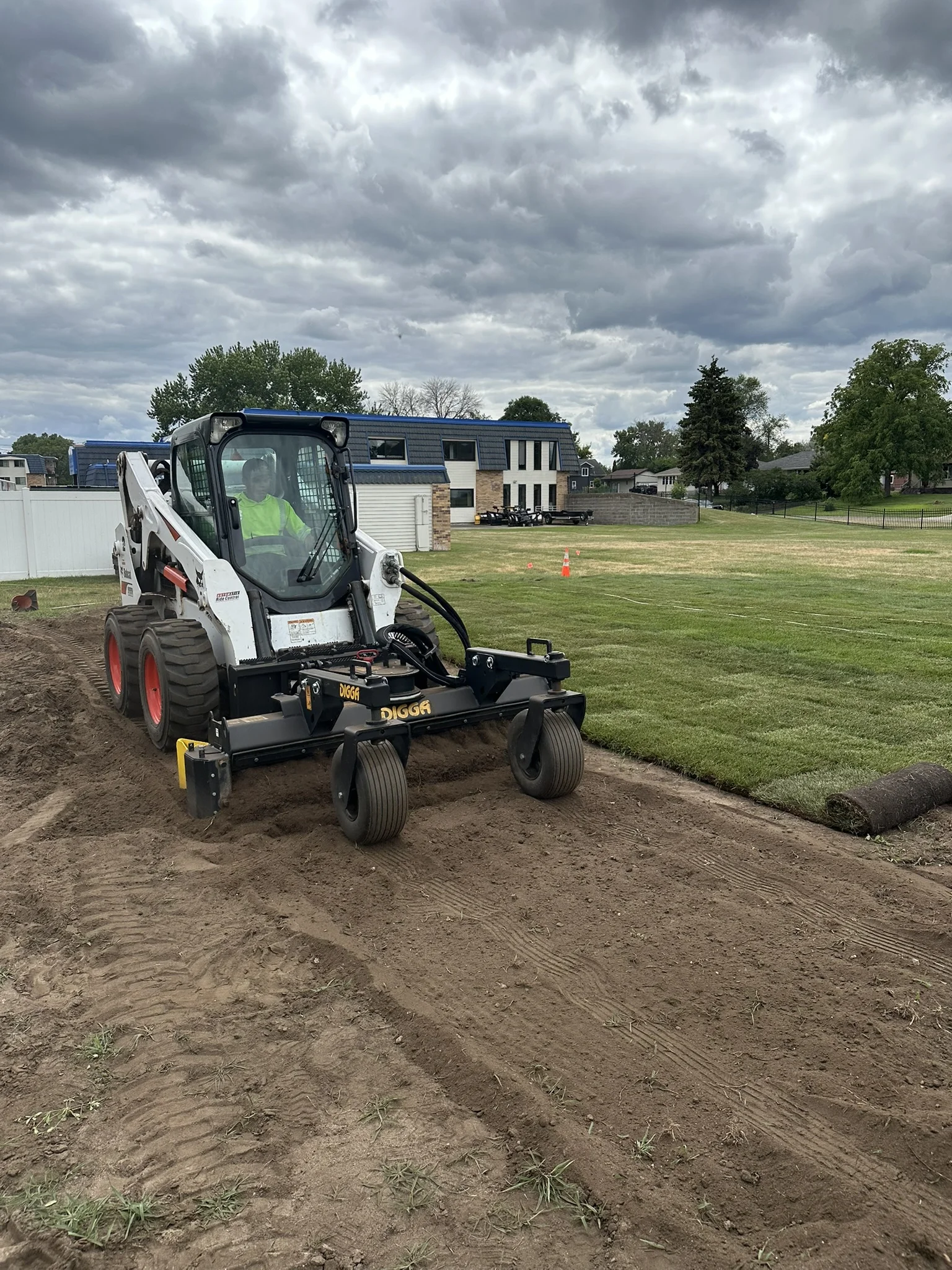 Clearline Outdoor crew tilling and grading soil with a skid steer attachment ahead of sod installation