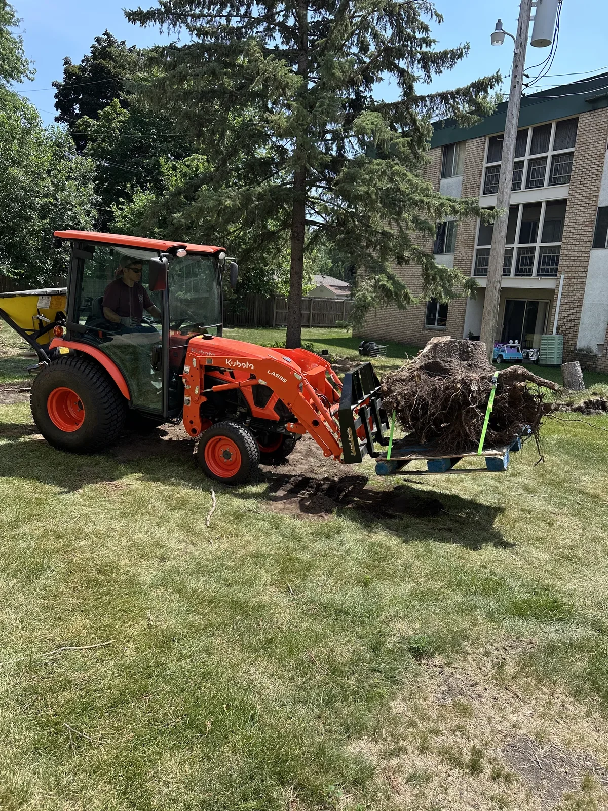 Kubota tractor hauling a removed tree stump at a multifamily property
