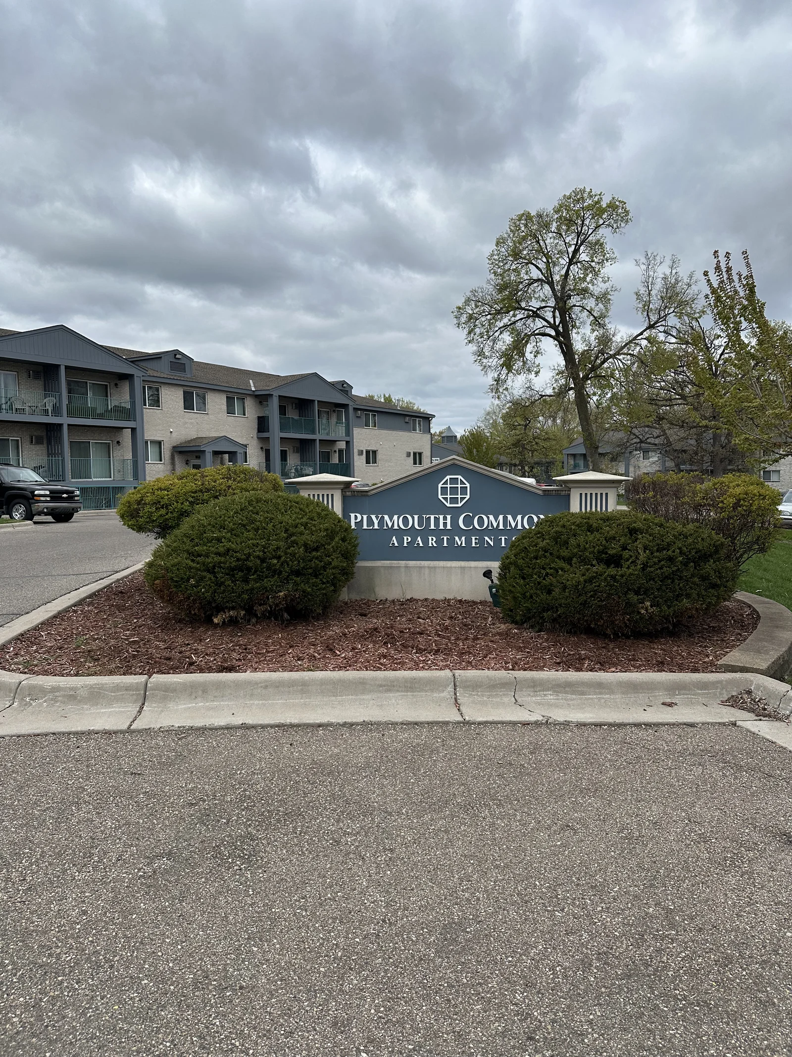 Plymouth Commons monument sign with thin mulch under an overcast sky before renovation