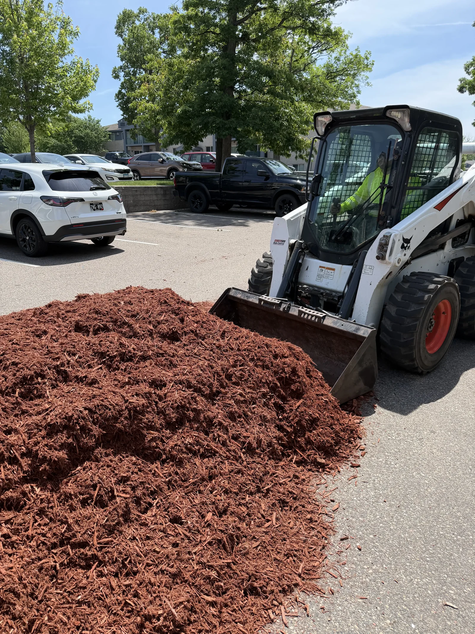 Skid steer scooping bulk mulch for the property-wide bed refresh at Plymouth Commons