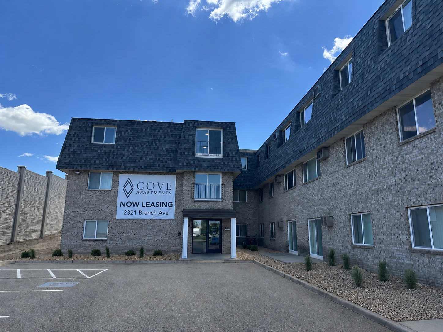 Cove Apartments building exterior with finished landscaping beds and Now Leasing signage in Anoka, Minnesota