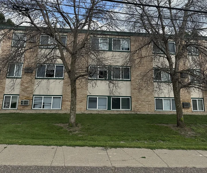 Two bare trees crowding the front of the building at Douglas Terrace Apartments in Crystal, Minnesota