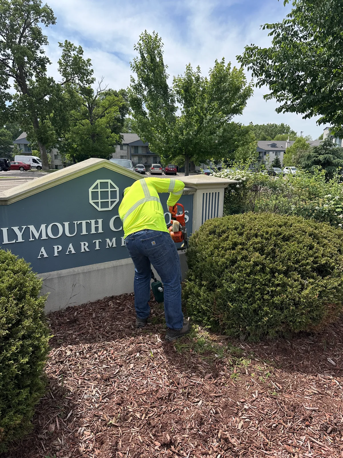 Clearline Outdoor crew member trimming shrubs at the Plymouth Commons Apartments entrance sign