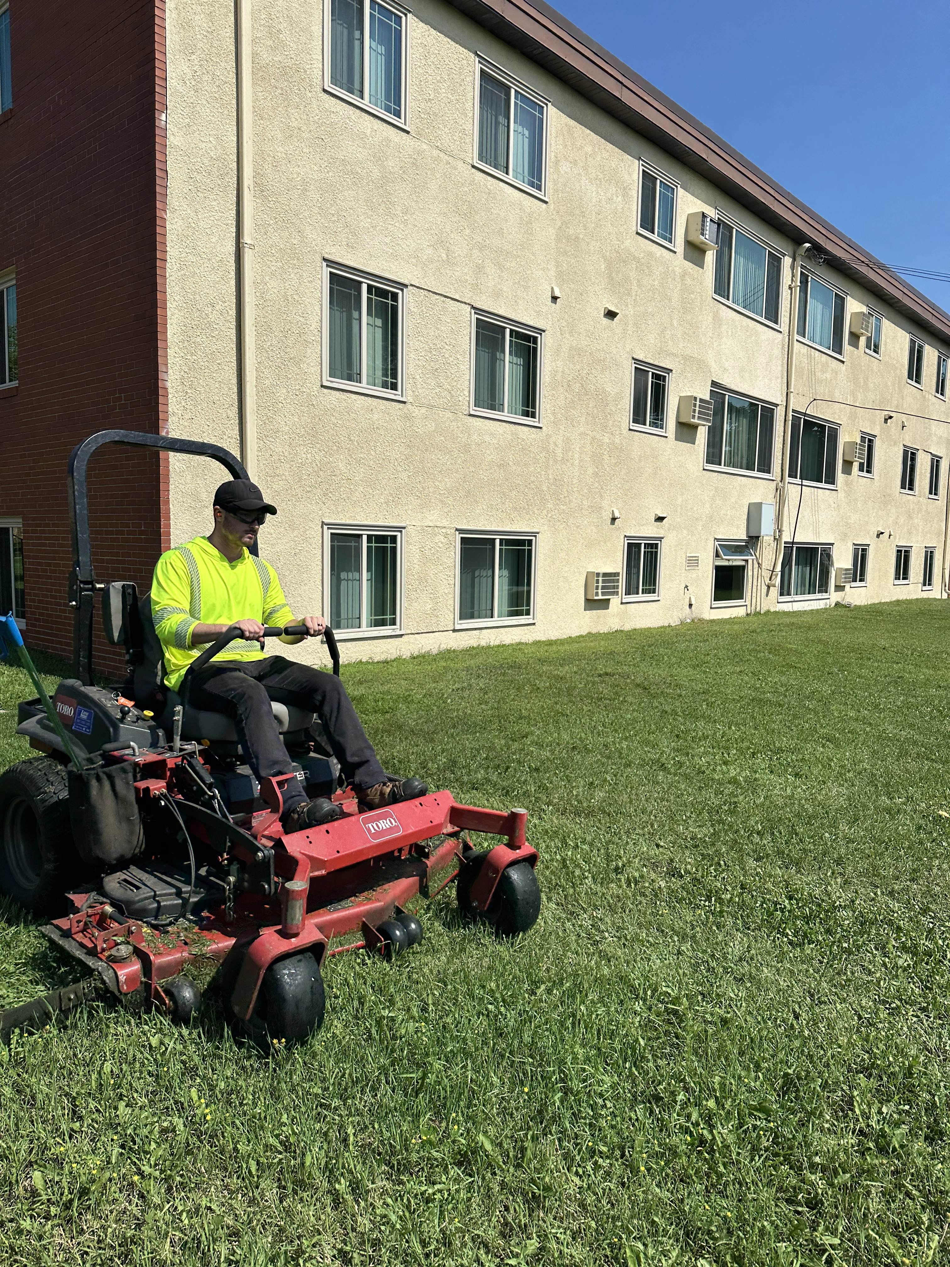 Clearline Outdoor crew member mowing apartment complex grounds on a zero-turn mower in the North Metro