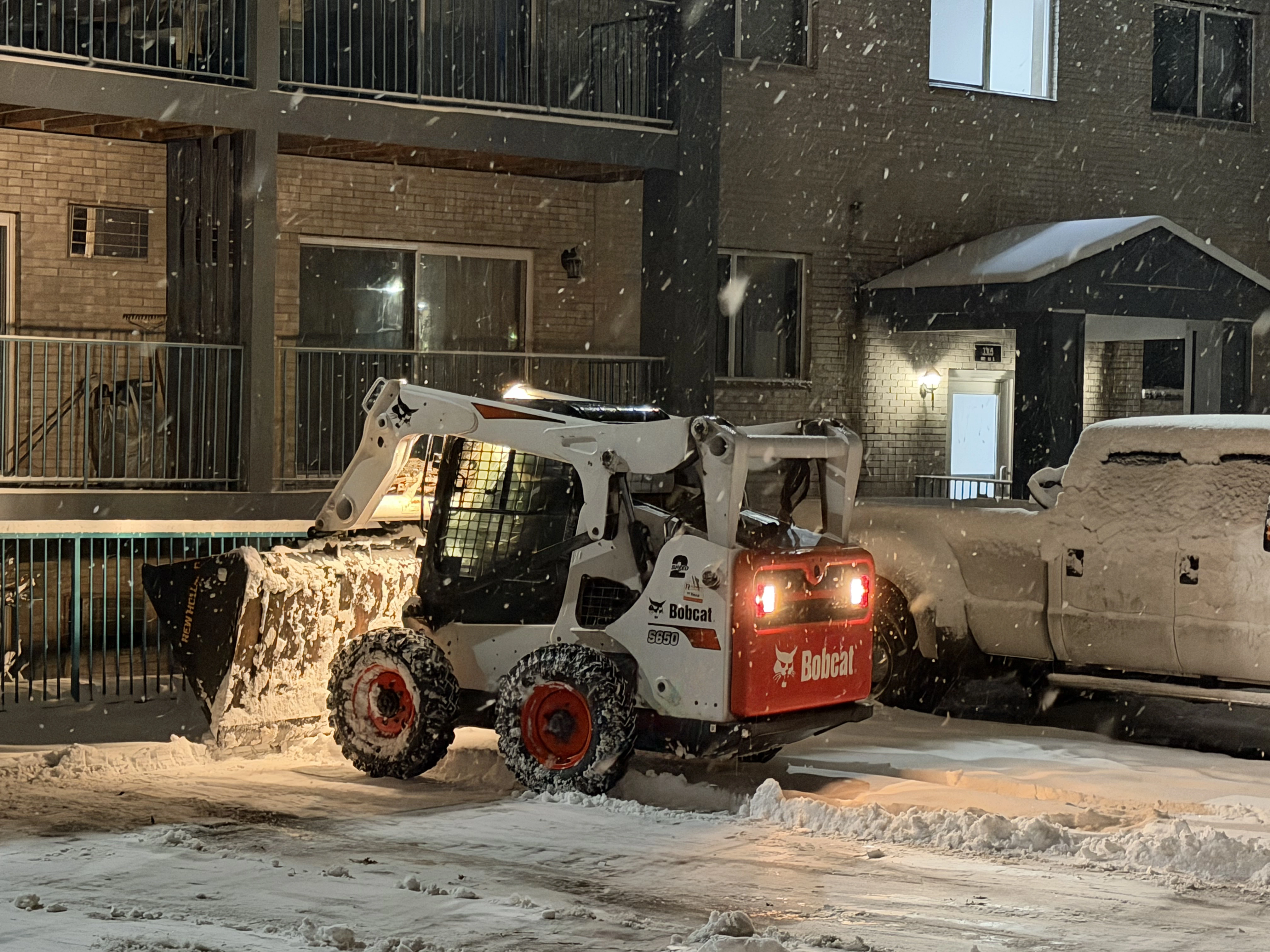Clearline Outdoor skid steer clearing snow at a multifamily property during a night storm in the North Twin Cities Metro